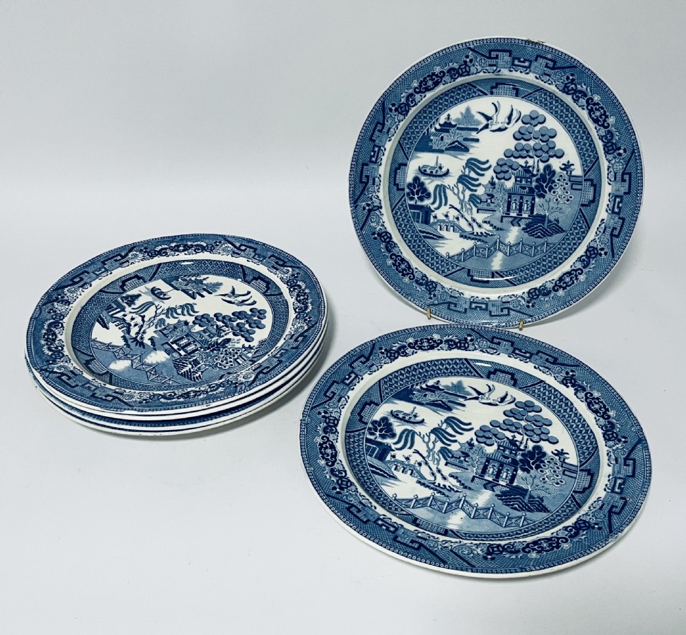 A set of six circular earthenware plates decorated with classic cobalt blue and white Willow Pattern transferware illustrations.