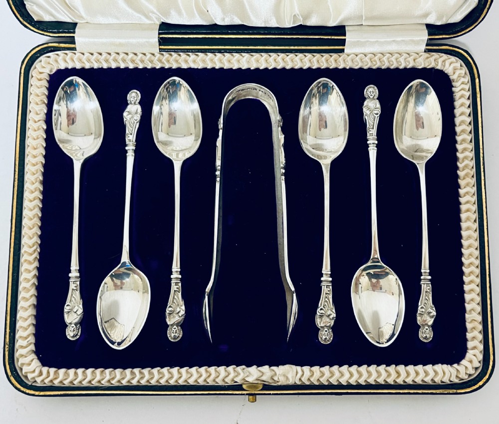 A cased set of six silver teaspoons and matching sugar tongs arranged in a blue velvet lined presentation box with cream satin lid. View II