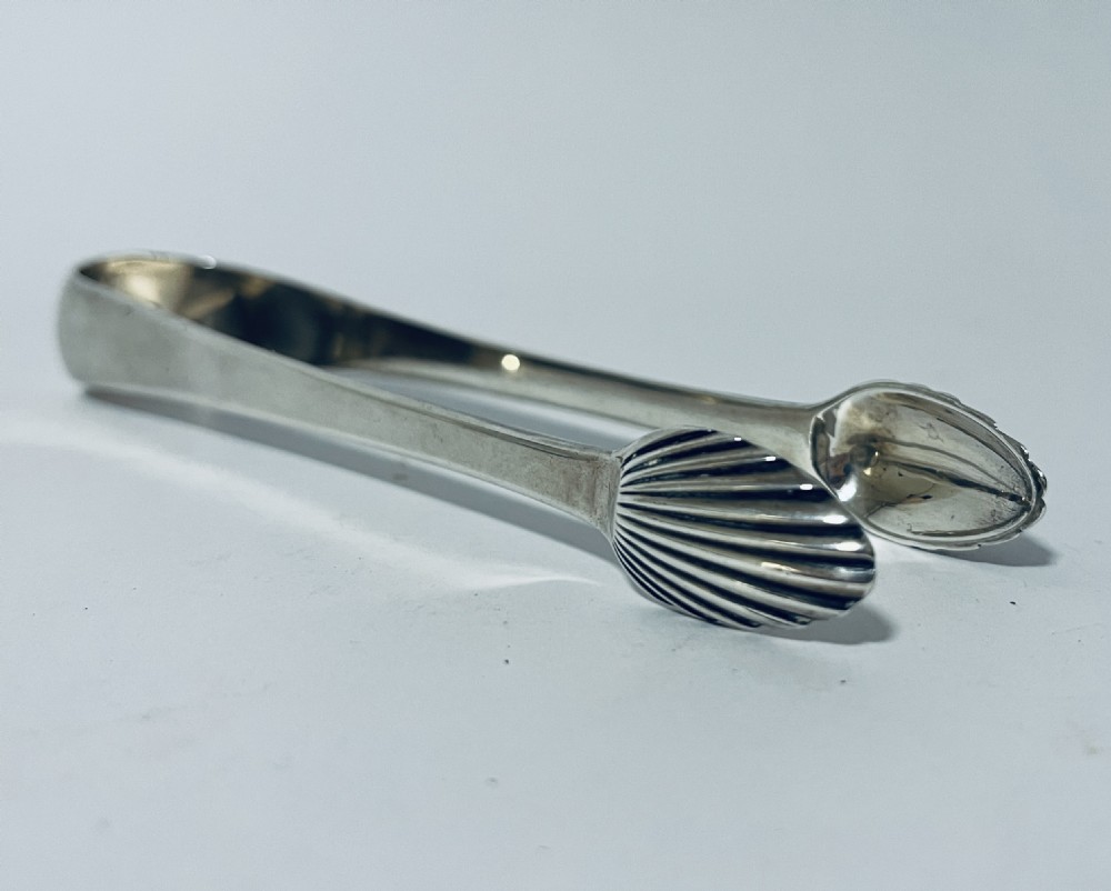 A pair of Georgian sterling silver sugar tongs featuring shell-shaped grips and smooth curved arms. View VI