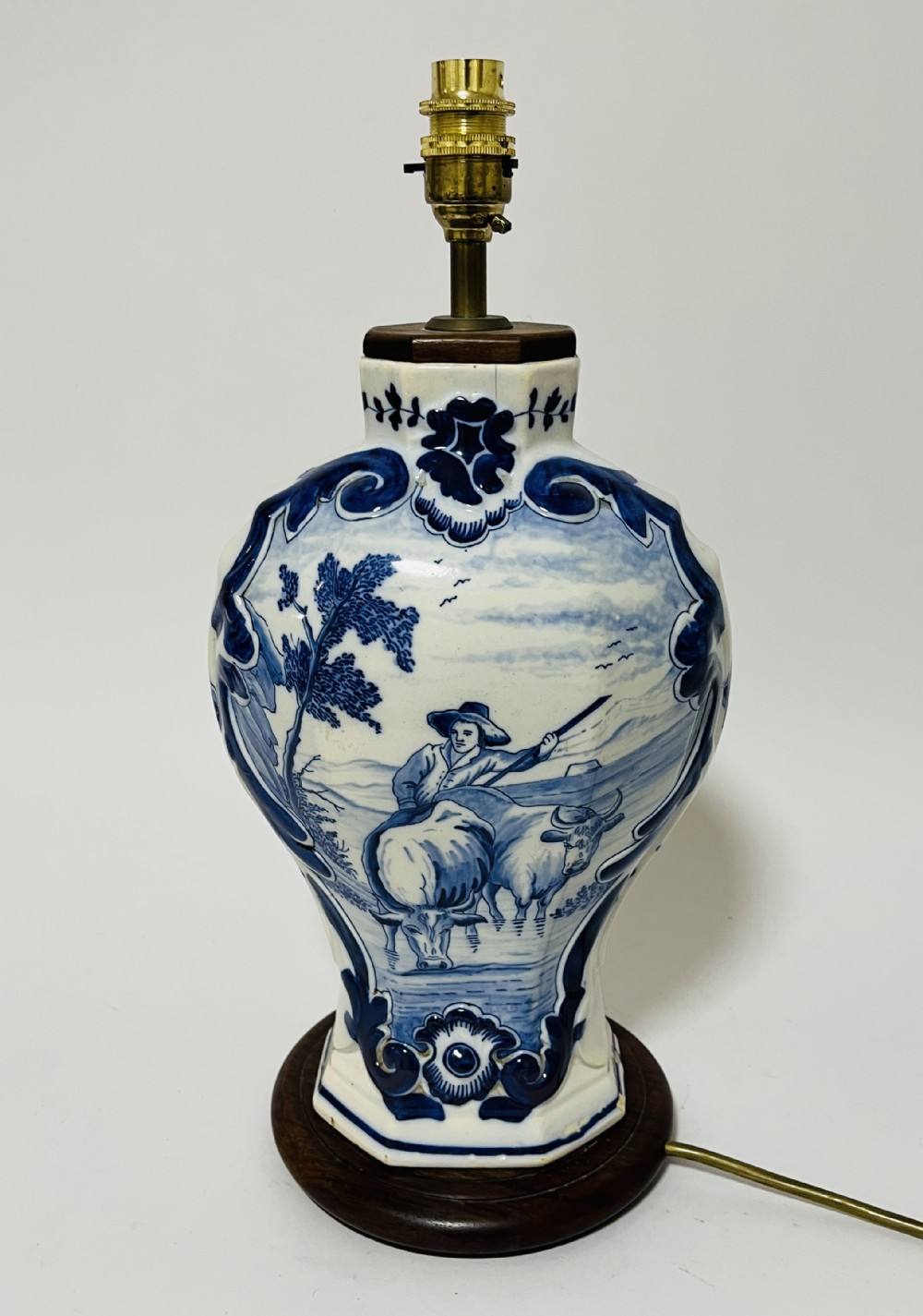 An 18th-century baluster-shaped Delftware ceramic vase decorated with blue and white pastoral scenes, mounted on a dark wooden plinth as a table lamp with brass fittings.