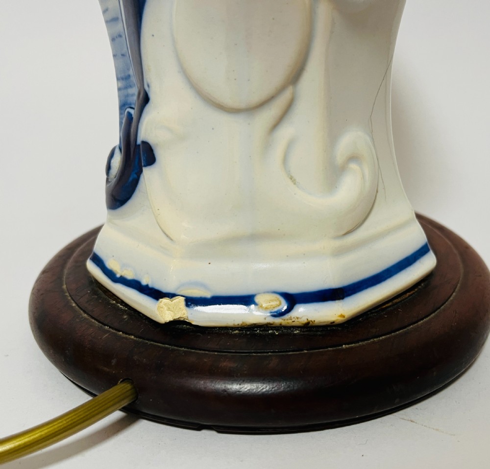 An 18th-century baluster-shaped Delftware ceramic vase decorated with blue and white pastoral scenes, mounted on a dark wooden plinth as a table lamp with brass fittings. View V