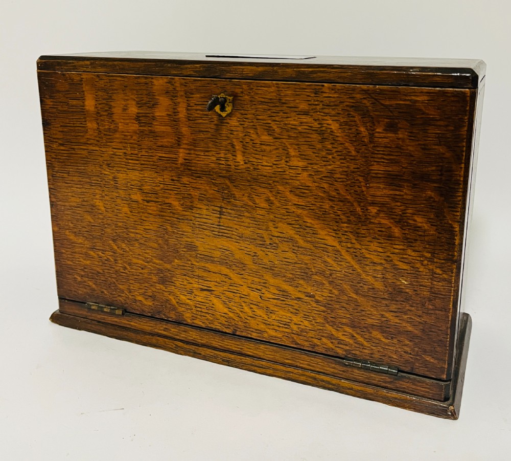 A rectangular Victorian dark oak stationery cabinet featuring a hinged drop-front, brass keyhole escutcheon, and an engraved metal plaque mounted on the top surface. View IX