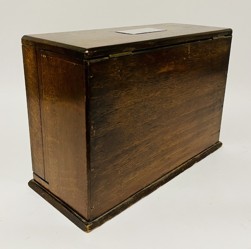 A rectangular Victorian dark oak stationery cabinet featuring a hinged drop-front, brass keyhole escutcheon, and an engraved metal plaque mounted on the top surface. View XVI