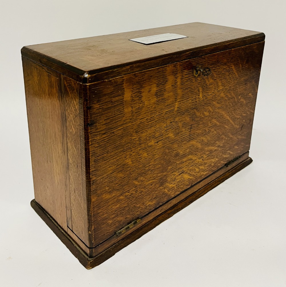 A rectangular Victorian dark oak stationery cabinet featuring a hinged drop-front, brass keyhole escutcheon, and an engraved metal plaque mounted on the top surface. View XVIII