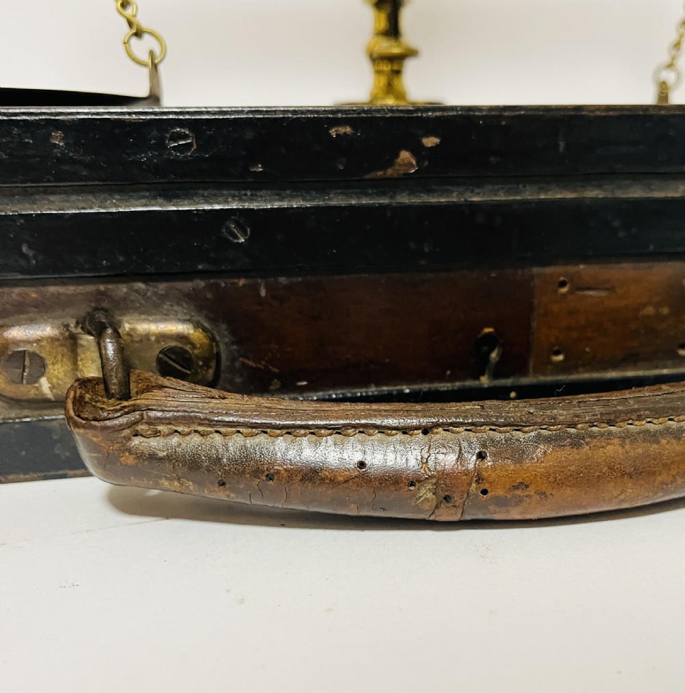 An antique brass balance scale stamped with County of Devon markings, resting on a black fitted transport case with two suspended brass pans. View XII
