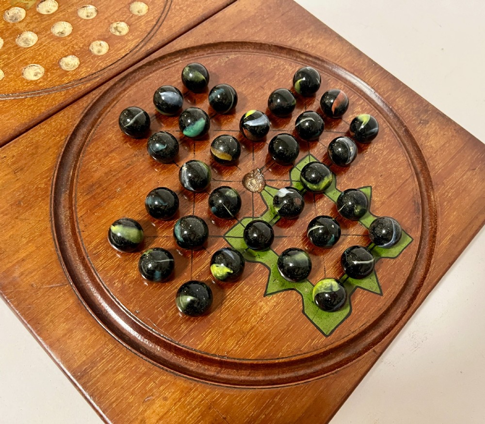 A two-panel antique mahogany solitaire games board featuring indented circular playing tracks alongside a collection of dark glass marbles. View II