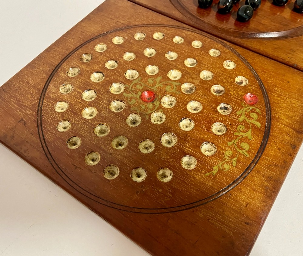 A two-panel antique mahogany solitaire games board featuring indented circular playing tracks alongside a collection of dark glass marbles. View III