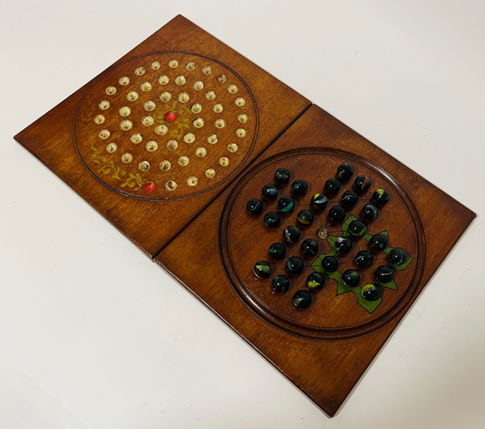 A two-panel antique mahogany solitaire games board featuring indented circular playing tracks alongside a collection of dark glass marbles. View V