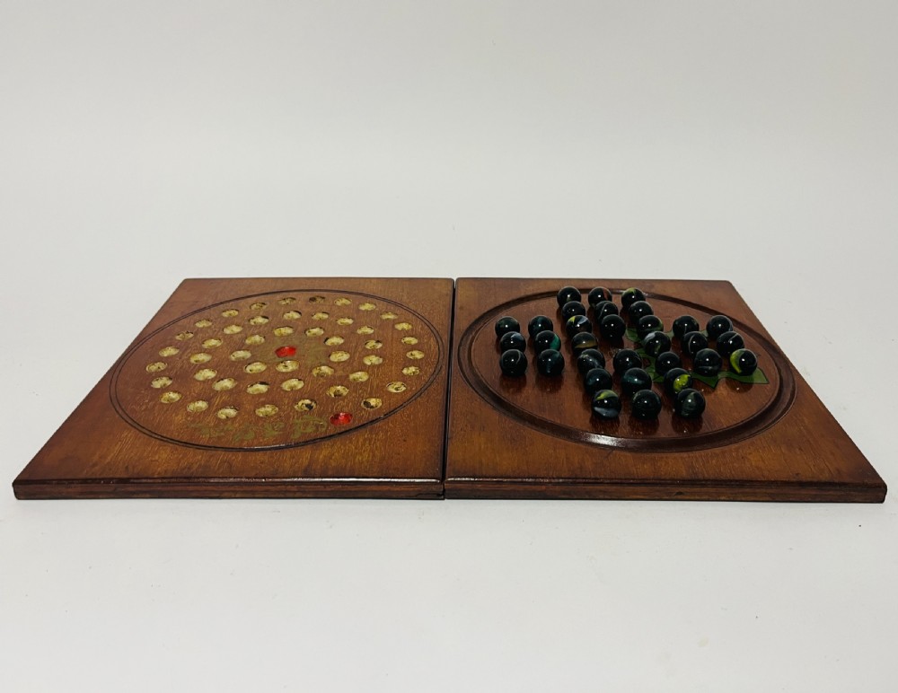 A two-panel antique mahogany solitaire games board featuring indented circular playing tracks alongside a collection of dark glass marbles. View VI