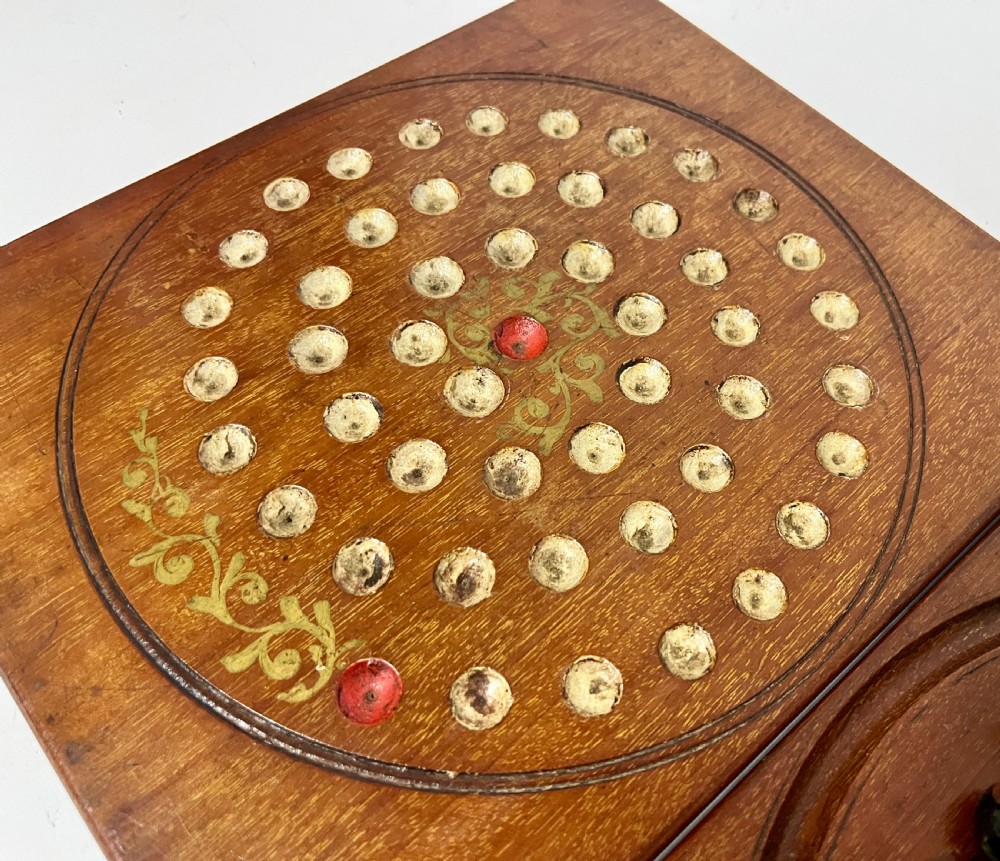 A two-panel antique mahogany solitaire games board featuring indented circular playing tracks alongside a collection of dark glass marbles. View VII