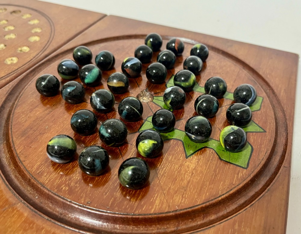 A two-panel antique mahogany solitaire games board featuring indented circular playing tracks alongside a collection of dark glass marbles. View VIII
