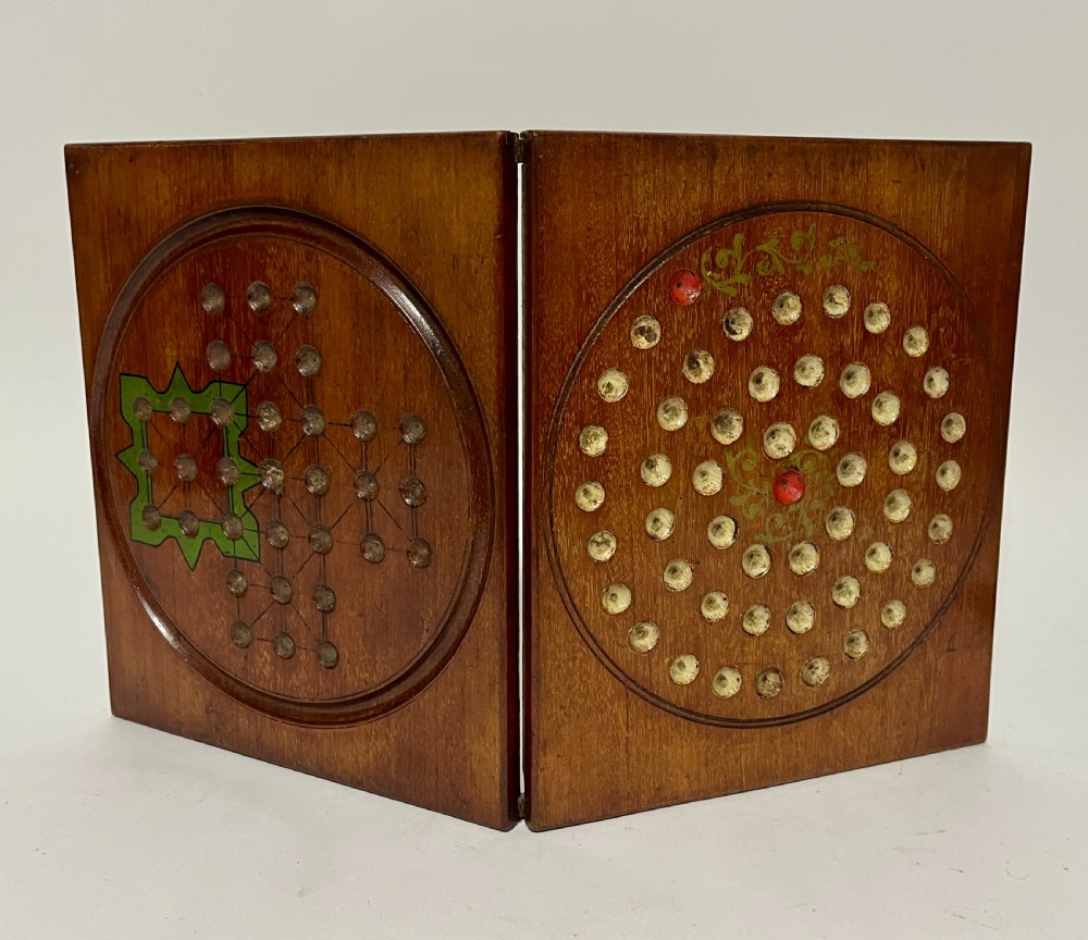A two-panel antique mahogany solitaire games board featuring indented circular playing tracks alongside a collection of dark glass marbles. View X