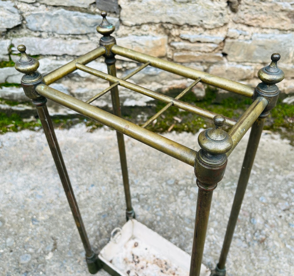 A Victorian brass stick stand featuring four upright posts with turned finials, a six-division top frame, and a painted metal drip tray at the base. View IX