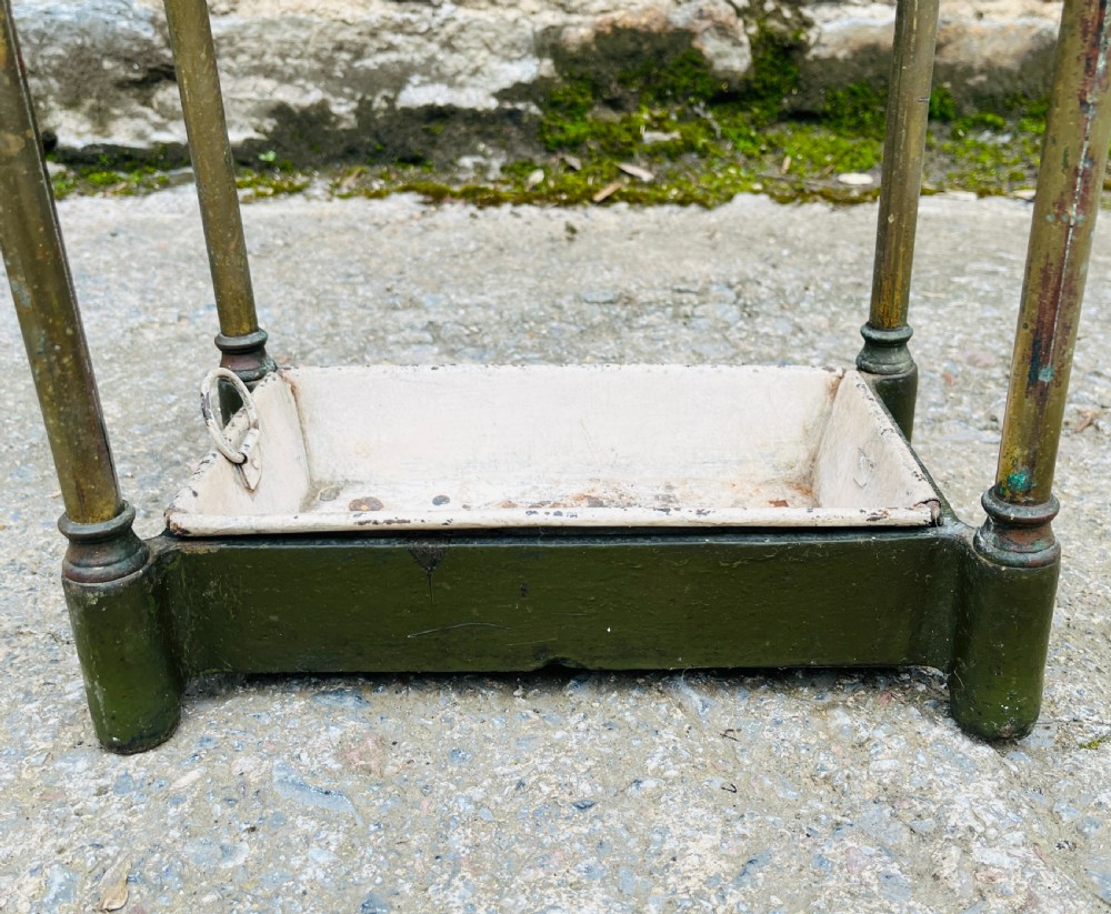 A Victorian brass stick stand featuring four upright posts with turned finials, a six-division top frame, and a painted metal drip tray at the base. View X