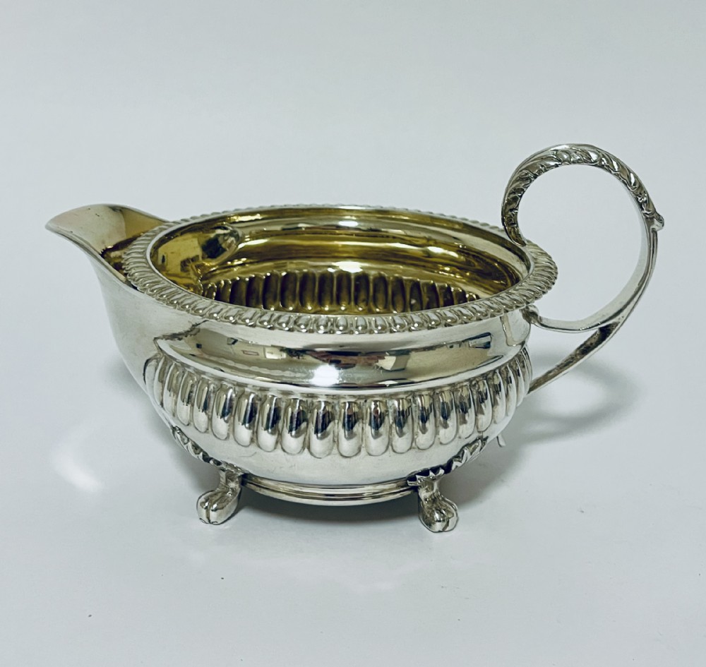 A Georgian sterling silver milk jug featuring a fluted lower body, gadrooned rim, single scroll handle, and gilt interior.