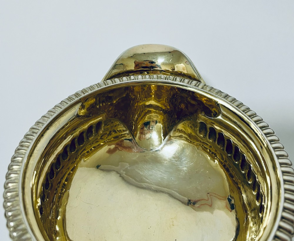 A Georgian sterling silver milk jug featuring a fluted lower body, gadrooned rim, single scroll handle, and gilt interior. View VI