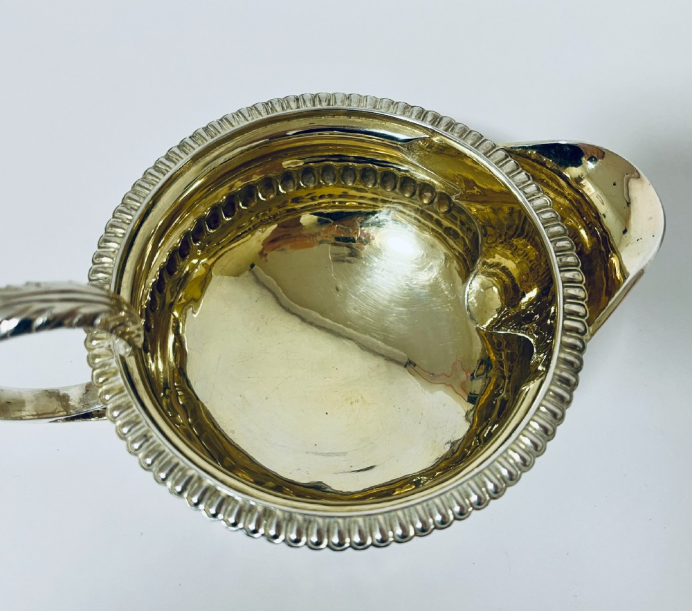 A Georgian sterling silver milk jug featuring a fluted lower body, gadrooned rim, single scroll handle, and gilt interior. View VII