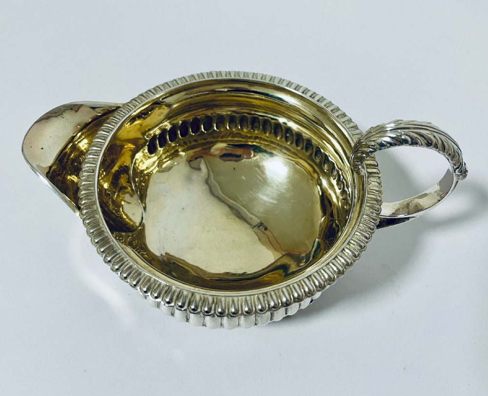A Georgian sterling silver milk jug featuring a fluted lower body, gadrooned rim, single scroll handle, and gilt interior. View VIII