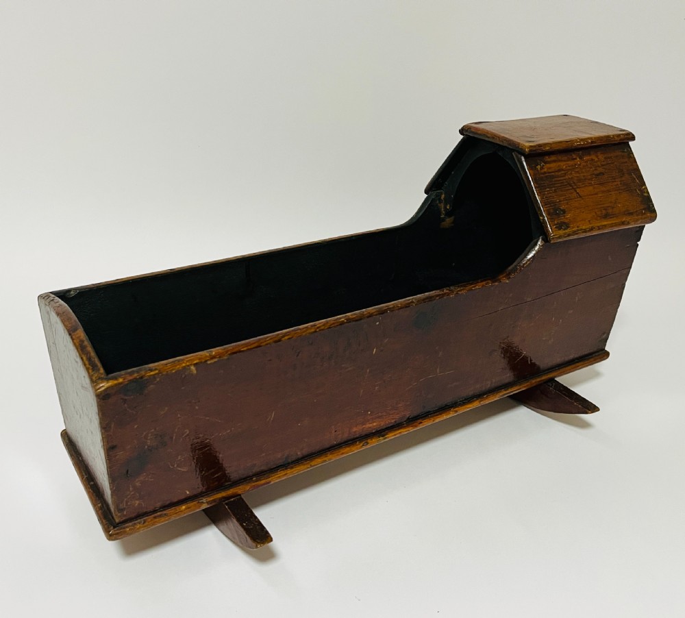 A dark stained pine miniature doll cradle featuring a hooded canopy and curved rockers.