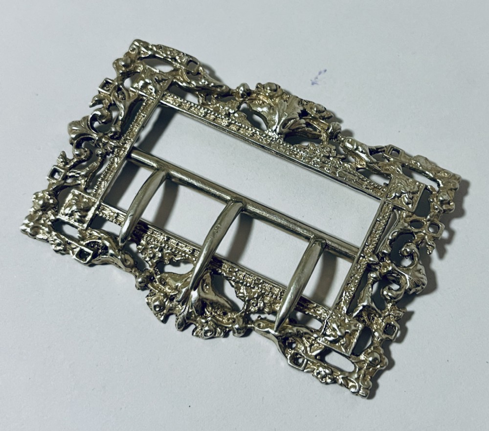 A rectangular Victorian silver belt buckle featuring intricate openwork foliate motifs and three central fastening prongs.