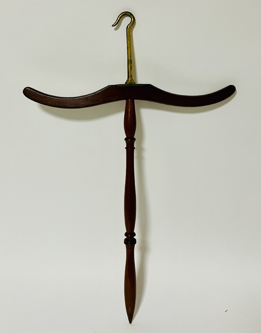 An antique dark mahogany gown and wig hanger featuring a contoured wooden shoulder bar, a turned central spindle, and a brass hook.