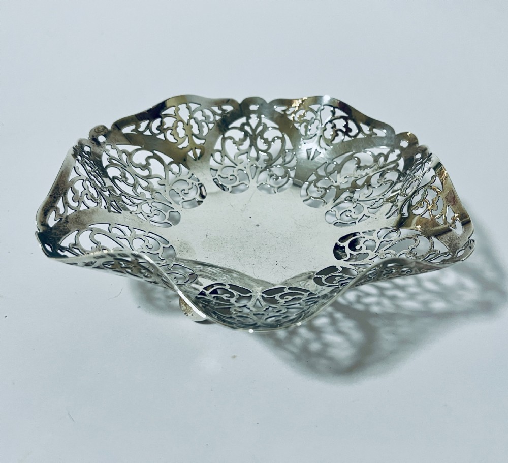 A small round silver bonbon dish featuring elaborate openwork pierced scroll motifs, a wavy scalloped rim, and ball feet. View III
