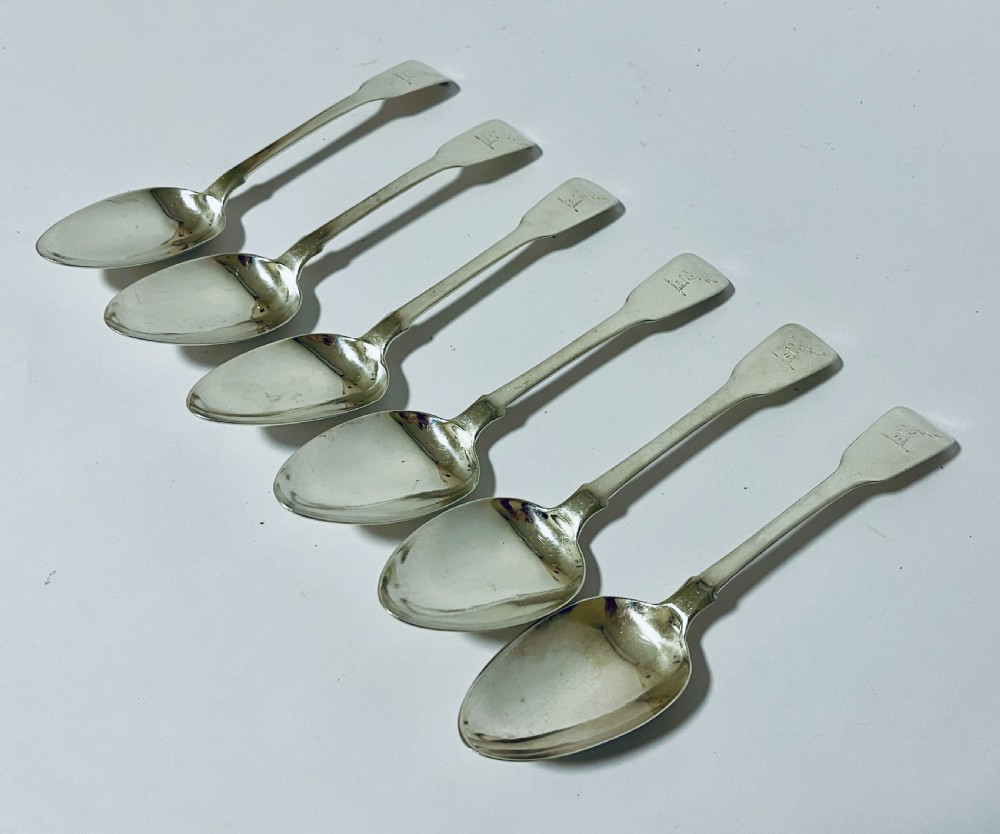 A set of six Georgian sterling silver tablespoons with oval bowls and engraved initial terminals laid out diagonally.