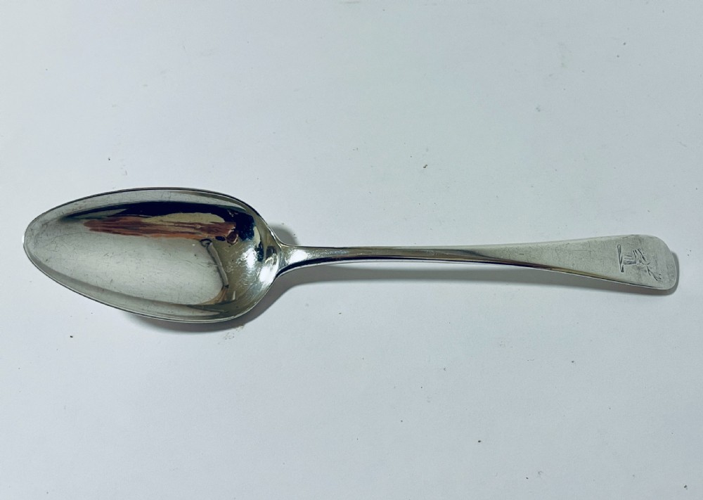 An 18th-century sterling silver serving spoon featuring a plain oval bowl and an engraved heraldic crest on the flat handle terminal.