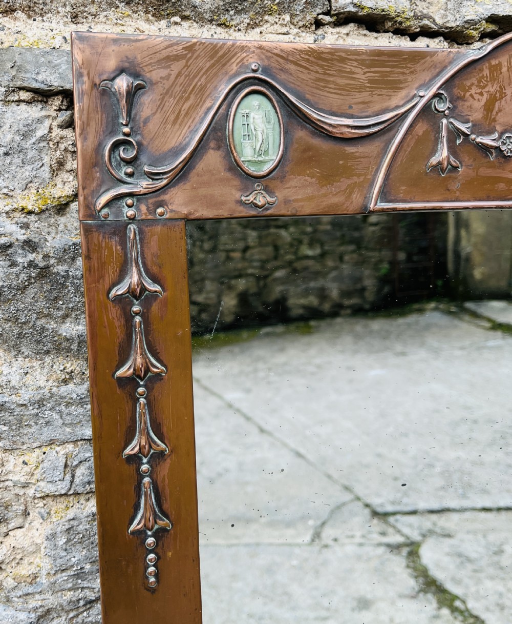 A rectangular Arts and Crafts wall mirror with an embossed copper frame featuring classical festoon motifs, an arched crest, and small green oval ceramic plaques. View II