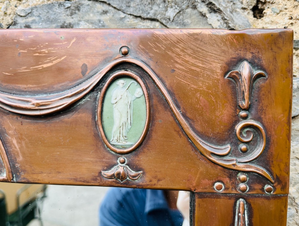 A rectangular Arts and Crafts wall mirror with an embossed copper frame featuring classical festoon motifs, an arched crest, and small green oval ceramic plaques. View V