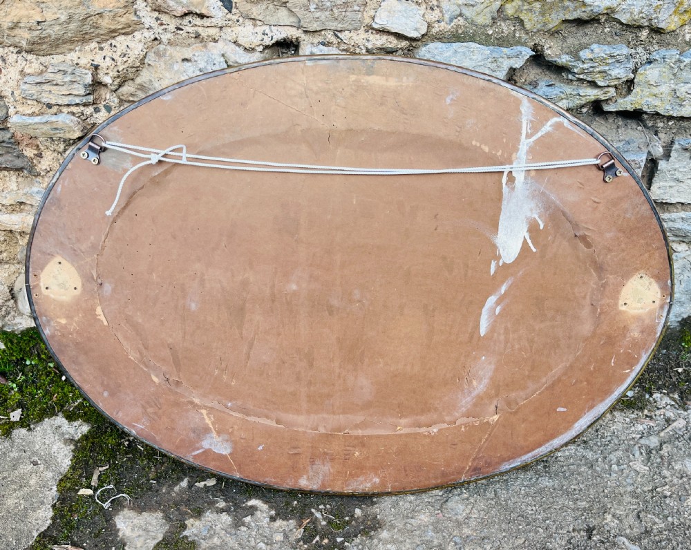 An oval wall mirror with a broad hammered brass frame featuring raised scroll motifs on the left and right sides. View IX