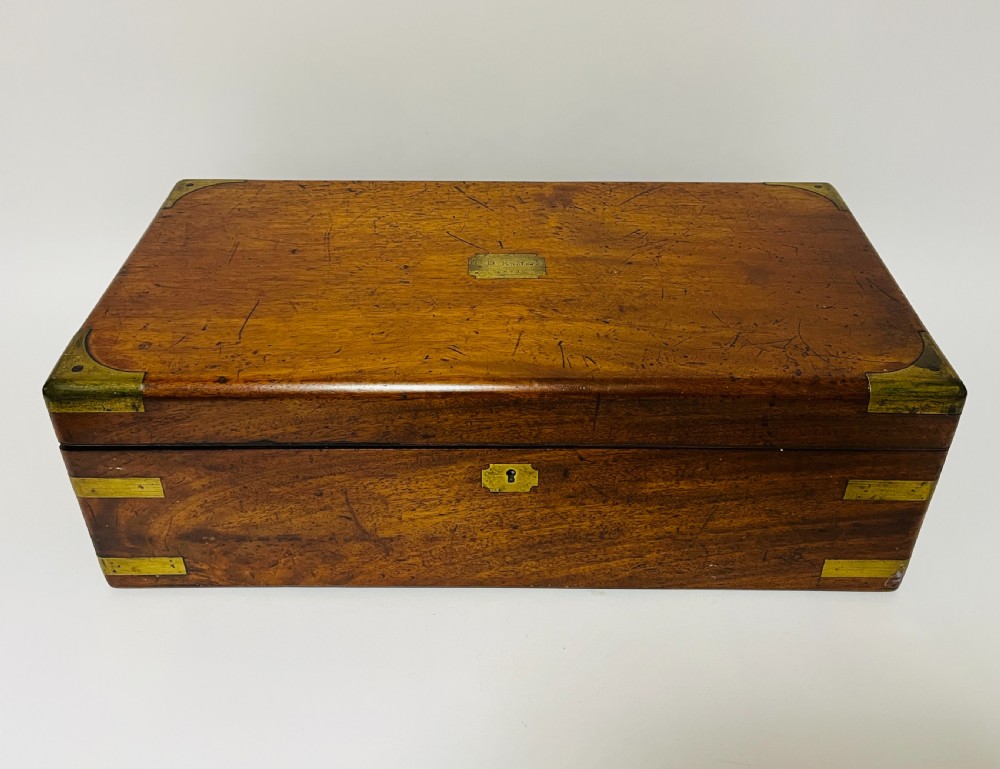 A rectangular mahogany wooden writing slope featuring protective brass corner brackets, brass straps, a central brass plaque, and a brass keyhole escutcheon.