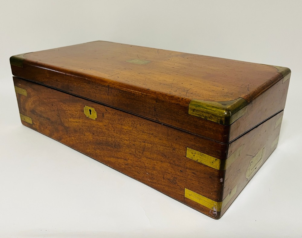 A rectangular mahogany wooden writing slope featuring protective brass corner brackets, brass straps, a central brass plaque, and a brass keyhole escutcheon. View XI
