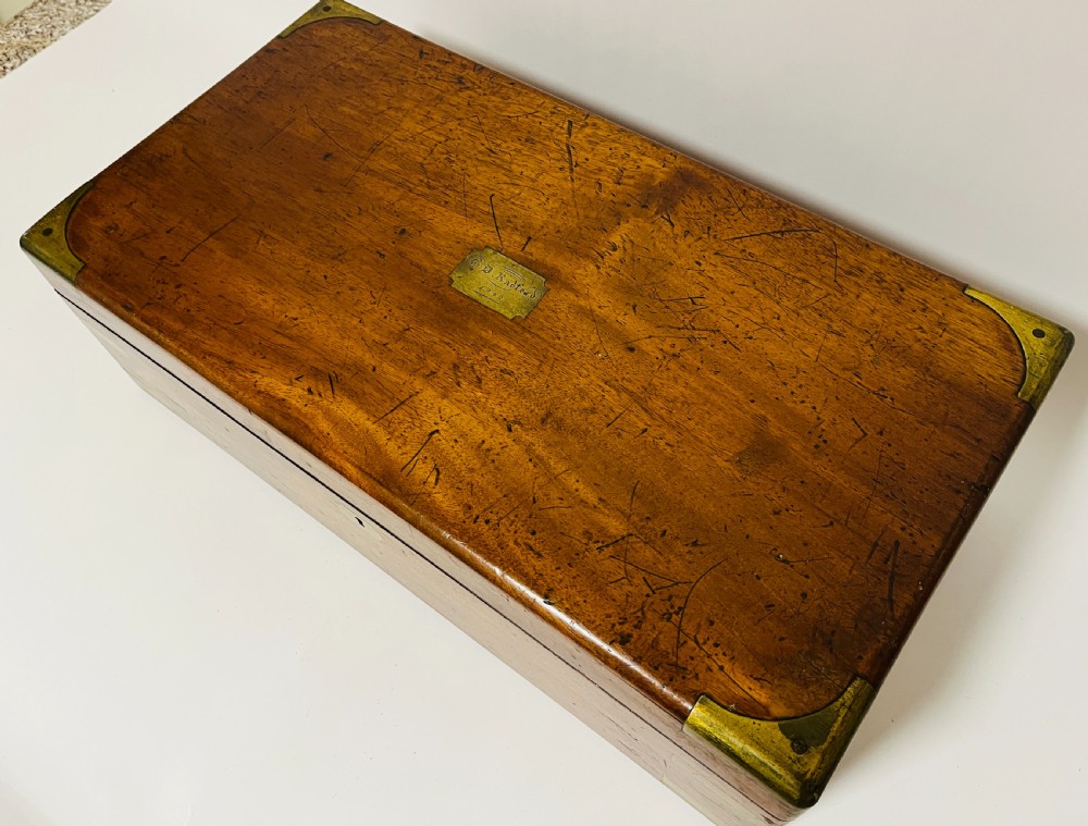 A rectangular mahogany wooden writing slope featuring protective brass corner brackets, brass straps, a central brass plaque, and a brass keyhole escutcheon. View XII
