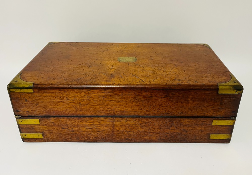 A rectangular mahogany wooden writing slope featuring protective brass corner brackets, brass straps, a central brass plaque, and a brass keyhole escutcheon. View XIV