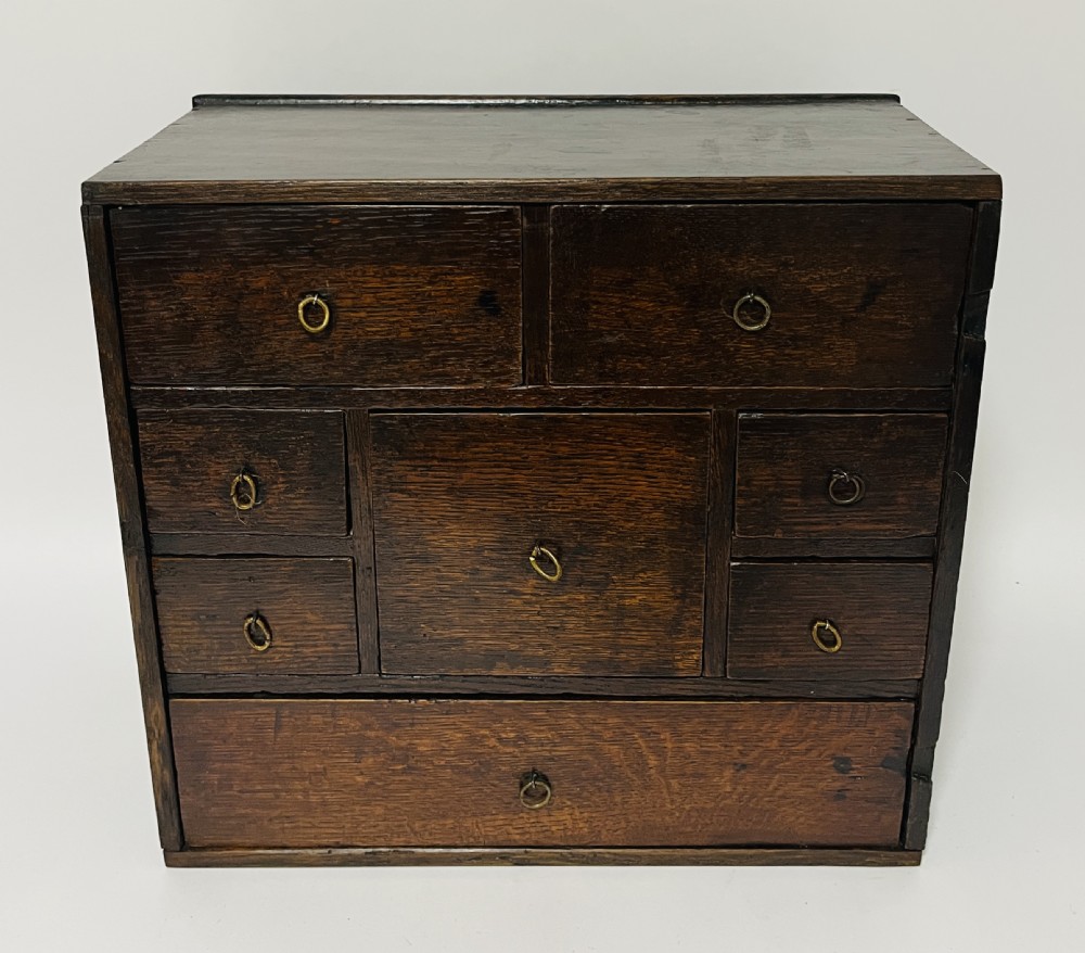 An 18th-century dark oak spice cabinet featuring multiple small drawers surrounding a central drawer, fitted with brass ring pulls.