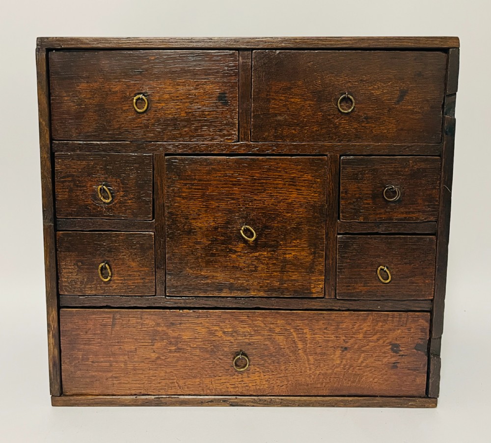 An 18th-century dark oak spice cabinet featuring multiple small drawers surrounding a central drawer, fitted with brass ring pulls. View IV