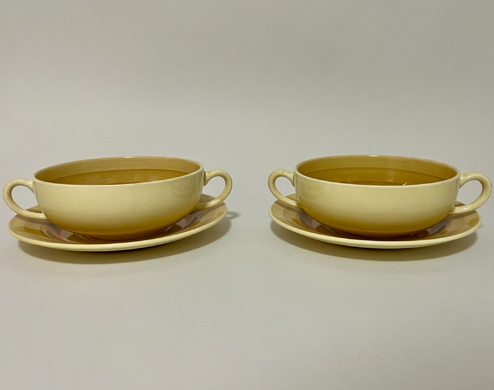 A pair of cream glazed earthenware soup coupes with twin handles and matching saucers decorated with ochre yellow, brown, and orange horizontal bands. View II