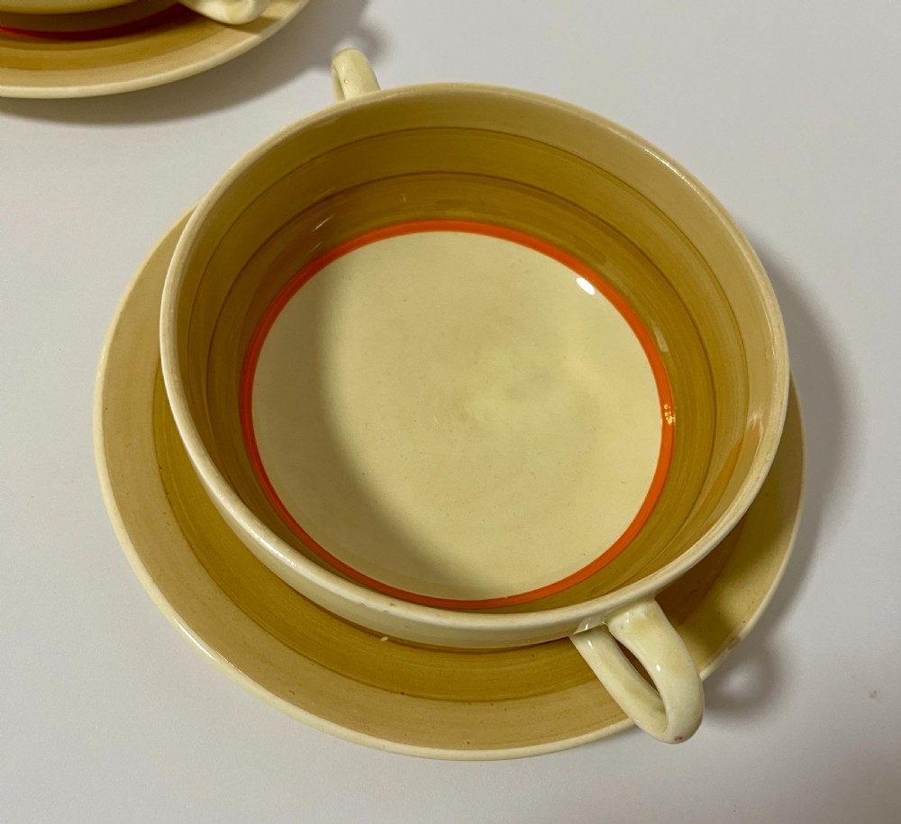 A pair of cream glazed earthenware soup coupes with twin handles and matching saucers decorated with ochre yellow, brown, and orange horizontal bands. View III