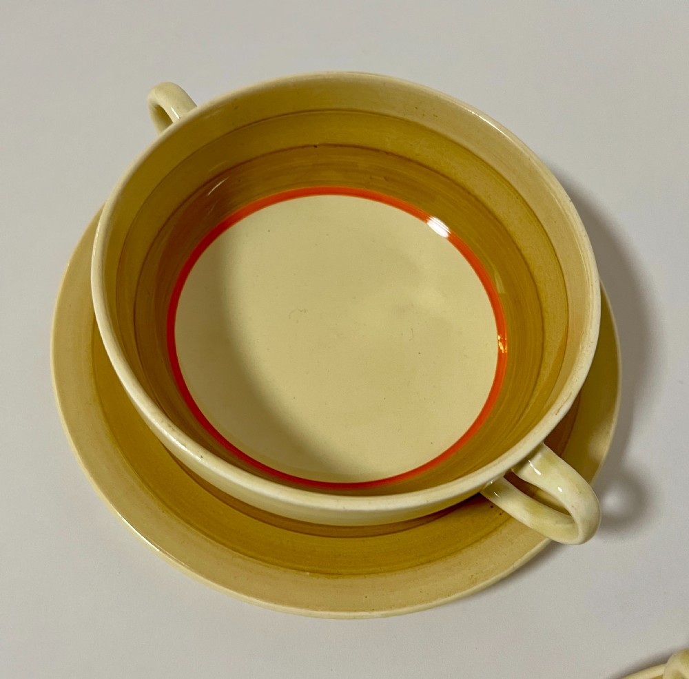 A pair of cream glazed earthenware soup coupes with twin handles and matching saucers decorated with ochre yellow, brown, and orange horizontal bands. View IV