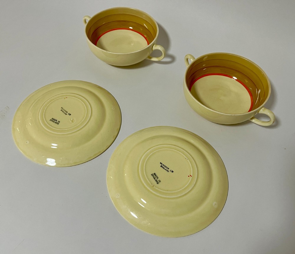 A pair of cream glazed earthenware soup coupes with twin handles and matching saucers decorated with ochre yellow, brown, and orange horizontal bands. View VI