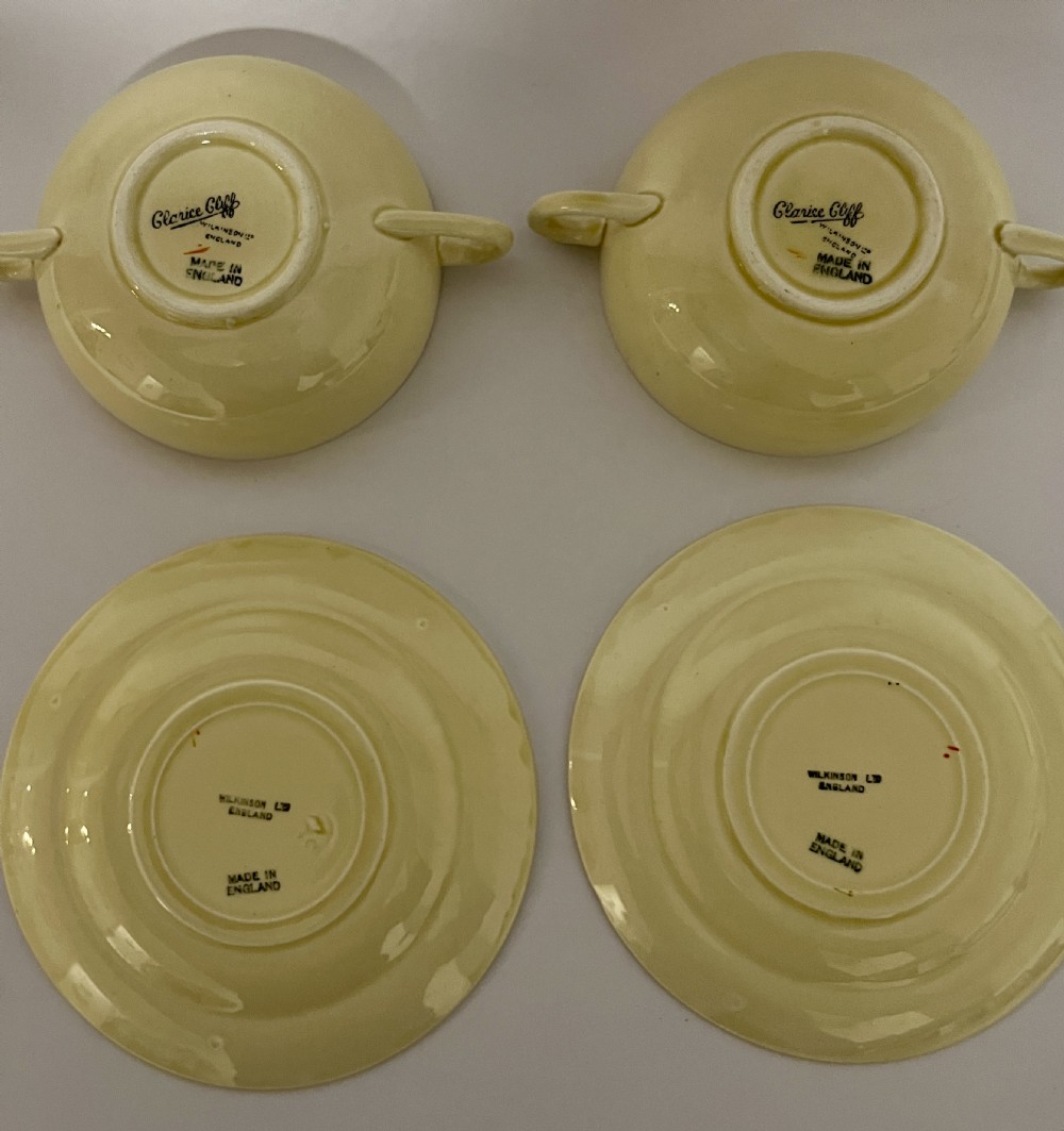 A pair of cream glazed earthenware soup coupes with twin handles and matching saucers decorated with ochre yellow, brown, and orange horizontal bands. View X