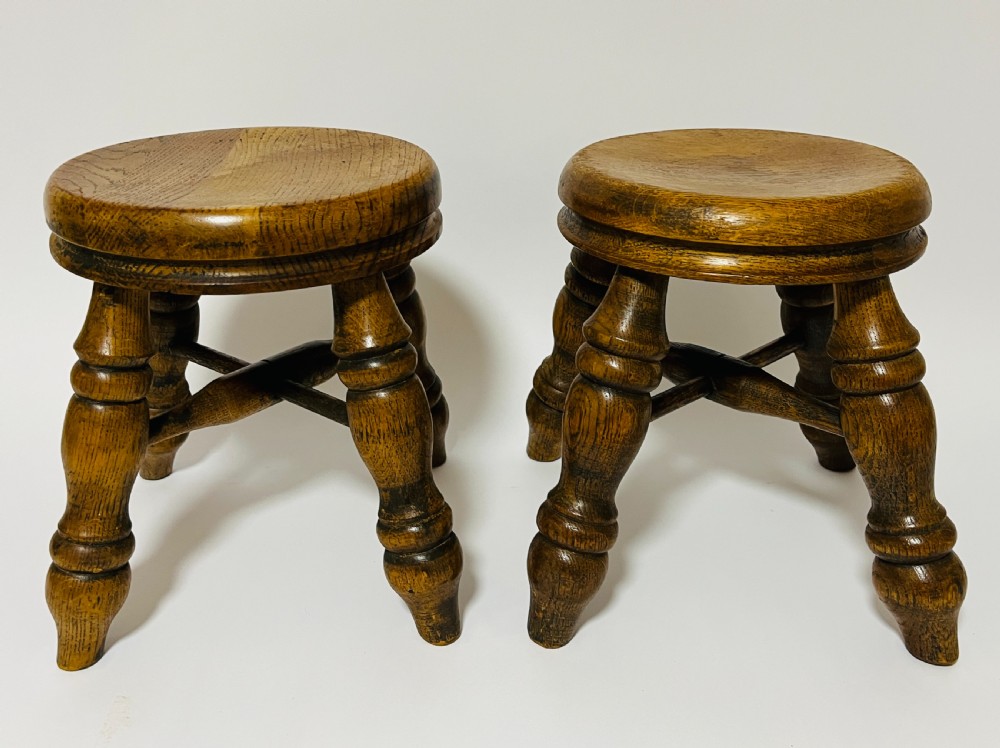 A pair of small antique oak stools with circular dished tops, turned baluster legs, and cross stretchers.