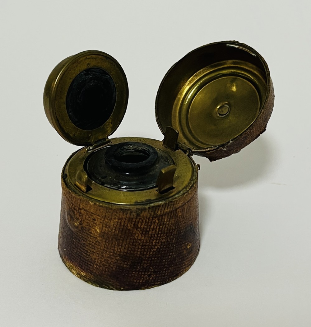 A 19th-century Victorian travelling inkwell encased in textured brown leather with a hinged brass lid open to reveal the interior stopper mechanism.