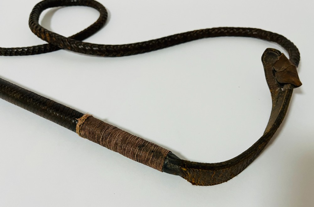 An antique hunting whip featuring a carved staghorn handle, a polished silver collar, a dark brown shaft, and a braided leather thong. View II