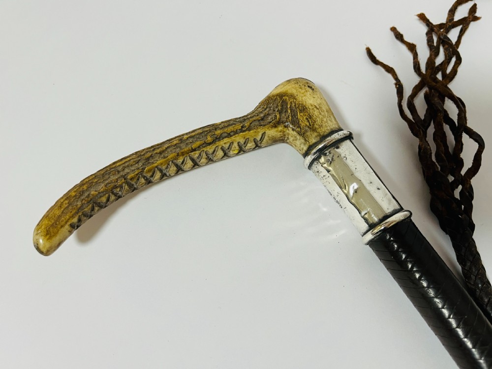 An antique hunting whip featuring a carved staghorn handle, a polished silver collar, a dark brown shaft, and a braided leather thong. View III