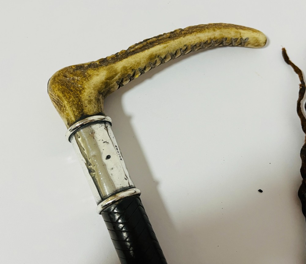 An antique hunting whip featuring a carved staghorn handle, a polished silver collar, a dark brown shaft, and a braided leather thong. View IV