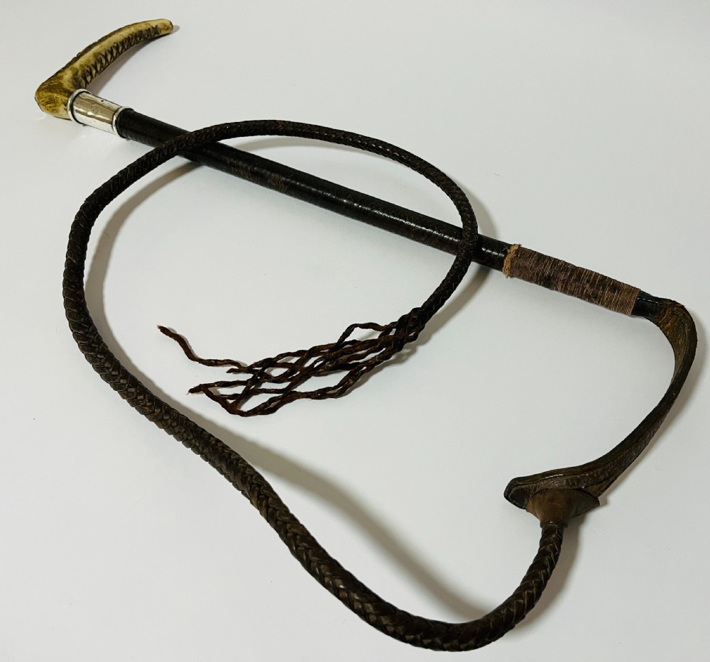 An antique hunting whip featuring a carved staghorn handle, a polished silver collar, a dark brown shaft, and a braided leather thong. View VII
