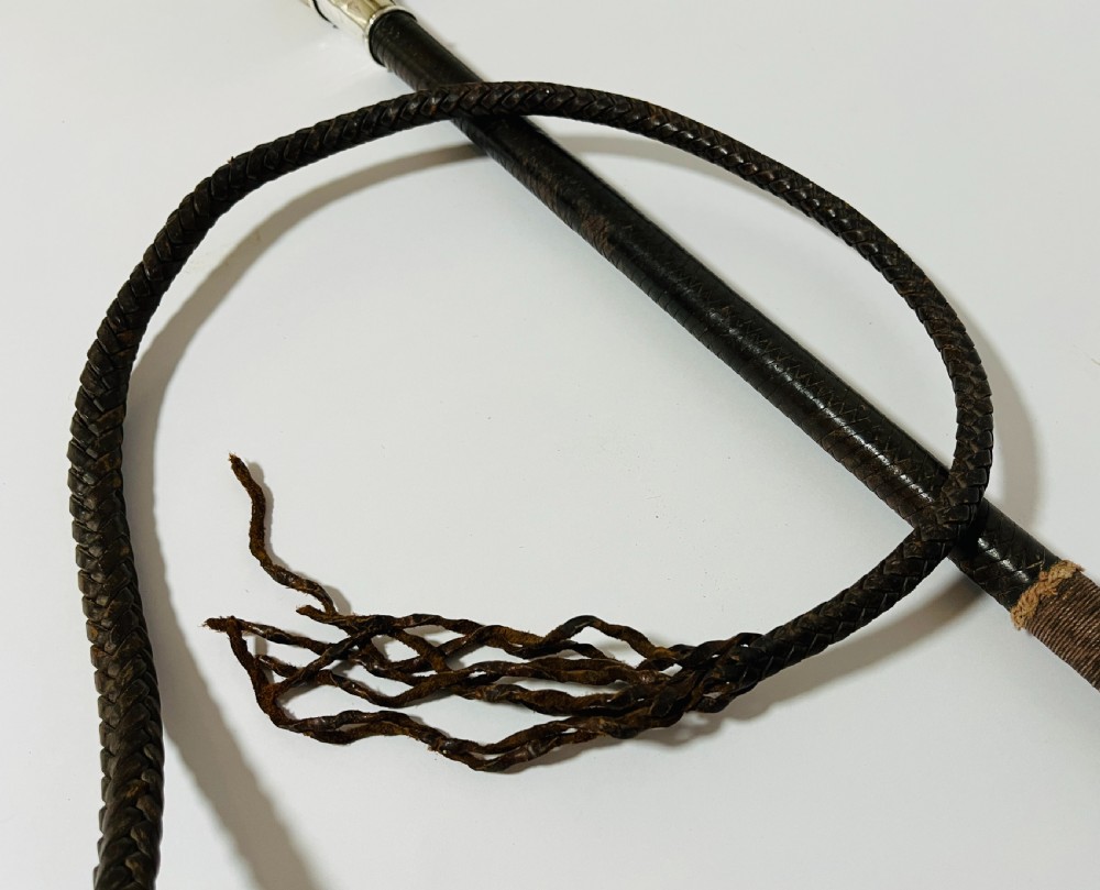 An antique hunting whip featuring a carved staghorn handle, a polished silver collar, a dark brown shaft, and a braided leather thong. View VIII