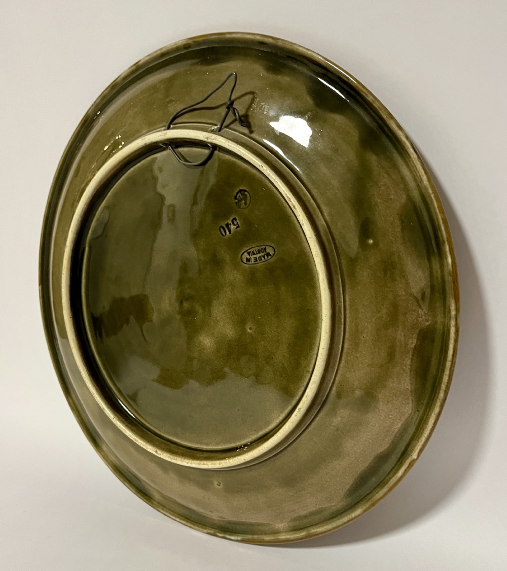 A circular Victorian majolica charger featuring relief figures of children and scrollwork in cobalt blue, ochre, and ivory glazes. View V